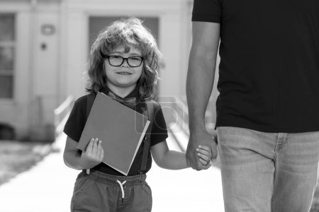 Photo for Parent and nerd pupil of primary school go hand in hand. Father holding hand of son with backpack outdoors, back to school - Royalty Free Image