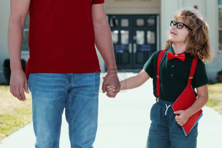 Foto de Retrato de un alumno nerd feliz sosteniendo a los profesores de la mano. Padre e hijo estadounidenses caminando por el parque escolar - Imagen libre de derechos