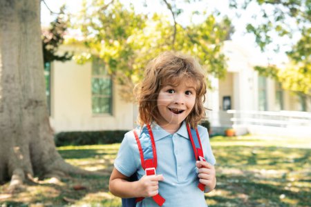 Téléchargez les photos : Elève de l'école primaire avec livre à la main. Écolier avec sac à dos près de l'école à l'extérieur. Début des leçons - en image libre de droit