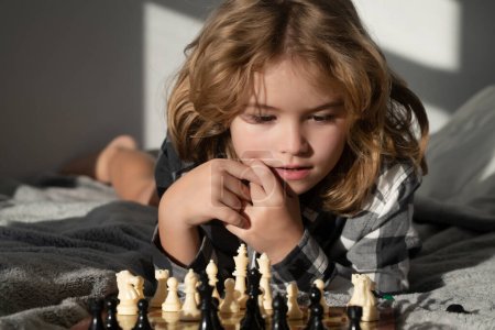 Téléchargez les photos : Intelligent concentré et pensant gamin jouant aux échecs. Développement du cerveau des enfants et jeu de logique. Enfants jouant aux échecs à la maison - en image libre de droit