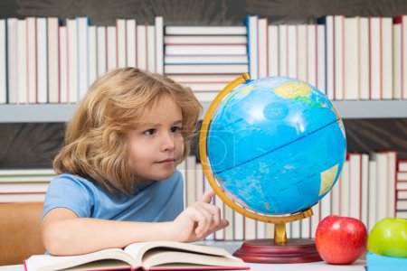 Téléchargez les photos : Explorer et découvrir. Étudiant regardant globe dans la bibliothèque de l'école primaire. Monde entier. Un gamin de l'école primaire avec un livre. Concept d'éducation et d'apprentissage - en image libre de droit