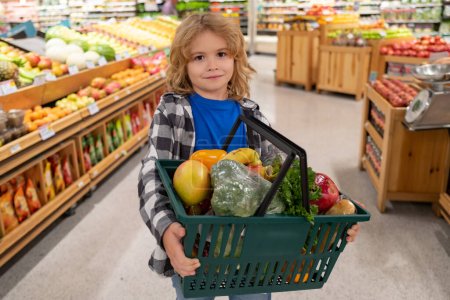 Photo for Portrait of child with shopping cart full of fresh vegetables in a food store. Supermarket shopping and grocery shop concept. Shopping kids. Child buying grocery in supermarket. hold shopping basket - Royalty Free Image