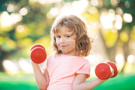 Photo for Fitness child. Portrait of sporty little boy with dumbbells in park. Gym workout. Child sportsman, childhood activity. Kids sport and Fitness - Royalty Free Image