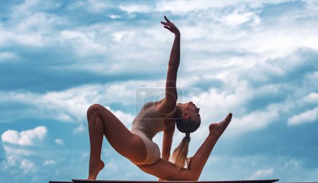 Photo for Woman stretching. Young girl practicing yoga, doing fit exercise, working out. Cloudy sky background - Royalty Free Image