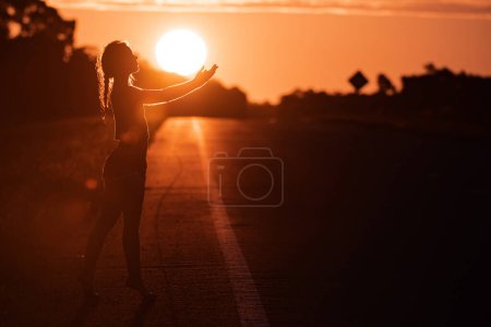 Photo for Black silhouette of pretty girl or beautiful woman, sexy slim model, with long hair poses on sea beach at sunset outdoors on yellow sky background. - Royalty Free Image