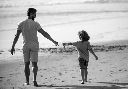 Foto de Padre e hijo caminando en la playa de verano. Papá y el niño tomados de la mano y caminando juntos - Imagen libre de derechos
