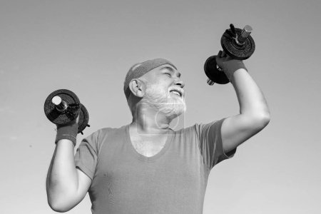 Photo for Old mature man exercising with dumbbell. Portrait of senior man holding dumbbell. Old man holding his hands in front of him while lifting dumbbells - Royalty Free Image