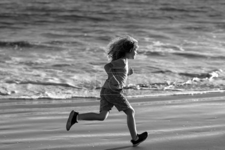 Foto de Niño corriendo a través del agua cerca de la orilla a lo largo de la playa. Un niño corre a lo largo de la costa. Resto de niños en vacaciones de verano. Deportes al aire libre y fitness para niños - Imagen libre de derechos