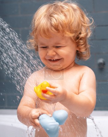 Téléchargez les photos : Douche d'enfant. Bébé heureux prenant un bain jouant avec des bulles de mousse. Petit enfant dans une baignoire. Enfant souriant dans la salle de bain avec canard jouet. Lavage et bain des nourrissons. Soins et hygiène des enfants - en image libre de droit