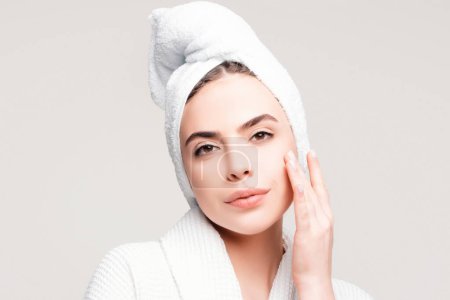 Téléchargez les photos : Jeune femme avec une serviette sur la tête crème sur le visage. Soin de la peau hydratant beauté spa concept de traitement - en image libre de droit
