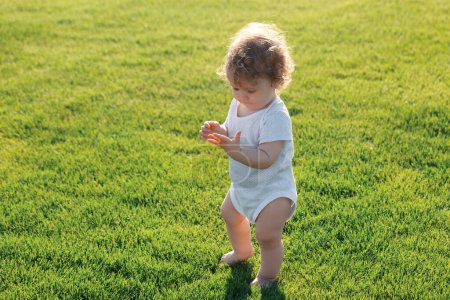 Foto de Pequeño bebé aprendiendo a gatear por la hierba. Concepto de niños meses. Niño feliz jugando en el patio de césped verde - Imagen libre de derechos