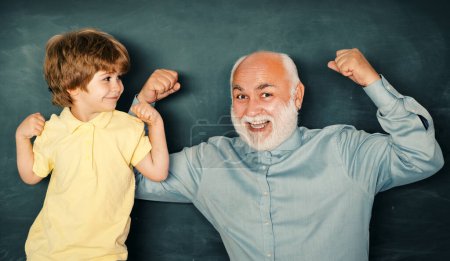 Photo for Elementary school kid and teacher with laptop in classroom at school. Grandfather with grandson learning lesson together. I love our moments in the school - remember time - Royalty Free Image