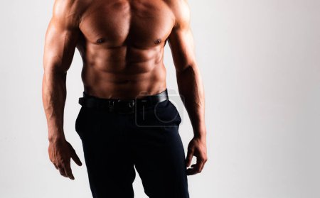 Male beauty and fashion concept. Muscular male model in trendy black pants posing over gray background.