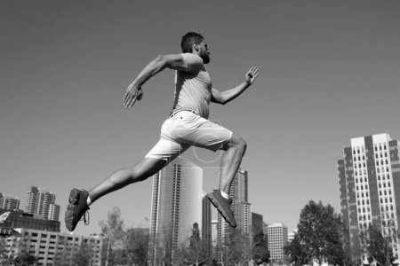 Foto de Joven atlético corriendo en la ciudad. Movimiento dinámico de salto. Jogger joven y activo corriendo. Concepto de deporte urbano - Imagen libre de derechos