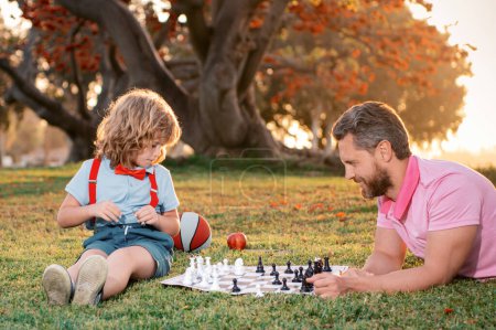 Téléchargez les photos : Joyeux famille en plein air. Père et fils jouant aux échecs dans le jardin d'automne - en image libre de droit