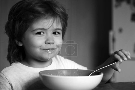 Téléchargez les photos : Un drôle de petit bébé mange. Bébé garçon heureux mange une cuillère de nourriture saine elle-même. Nourriture et boisson pour enfant. Un mignon gosse mange. Portrait d'un bel enfant prenant son petit déjeuner à la maison - en image libre de droit