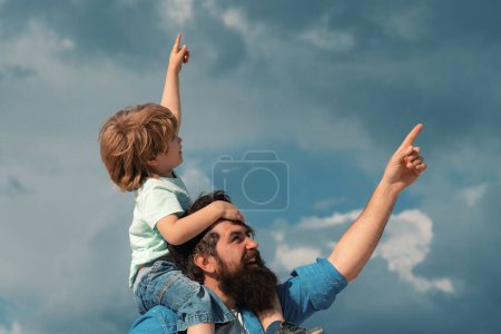 Téléchargez les photos : La fête des pères. Mignon garçon avec papa jouant en plein air. Joyeux enfant pointant sur fond de ciel d'été - en image libre de droit
