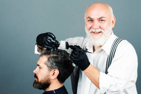 Photo for Process of a guy having his hair dyed at hairdresser. Hair coloring man agains grey hair. Professional senior hairdresser drying hair - Royalty Free Image