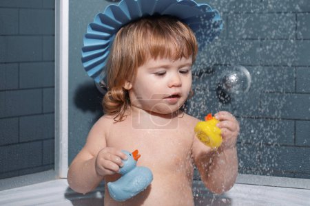 Téléchargez les photos : Il se baigne dans une douche. Petit bébé enfant se lave les cheveux dans le bain - en image libre de droit