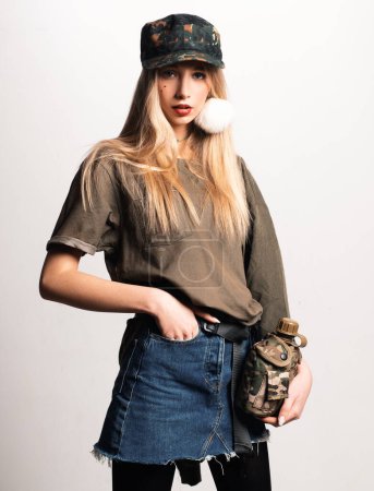 Photo for Magnificent white girl in military clothes posing with flask. Studio portrait of beautiful lady in jeans skirt looking on photographer - Royalty Free Image