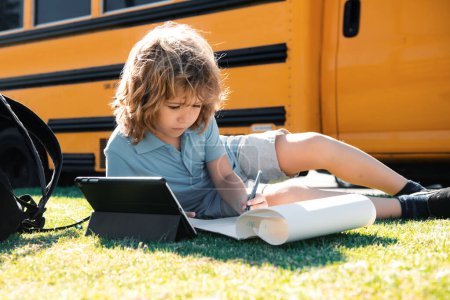 Téléchargez les photos : Elève écrivant ses devoirs avec tablette dans le parc de l'école. Concept d'enseignement à distance en ligne - en image libre de droit