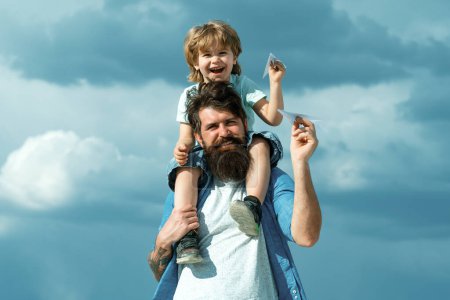 Photo for Generation. Father giving son ride on back in park. Father and son building together a paper airplane. Portrait of happy father giving son piggyback ride on his shoulders and looking up - Royalty Free Image