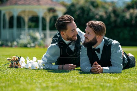 Foto de Pareja gay tendida en la hierba. Retrato de feliz pareja gay el día de la boda. Concepto de amor entre personas del mismo sexo y derechos LGBT - Imagen libre de derechos