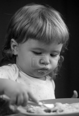 Téléchargez les photos : Enfant bébé avec une cuillère et une assiette dans la cuisine à la maison - en image libre de droit