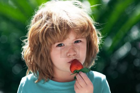 Foto de Niño feliz con fresas frescas sobre fondo verde veraniego - Imagen libre de derechos