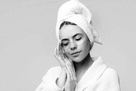 Photo for Woman applying eye patches. Calm relaxed woman has fresh healthy skin, keeps eyes shut, wears collagen patches under eyes, wears towel on head, gets facial treatment - Royalty Free Image