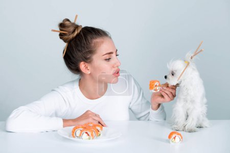 Foto de Estilo sushi japonés. Retrato de moda de chica modelo de belleza comiendo rollos de sushi, comida japonesa. Hermosa mujer sosteniendo palillos con sushi. Sexy dama con mascota perro anuncio - Imagen libre de derechos