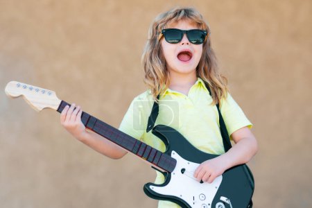 Foto de Un chico con guitarra. Divertido pequeño músico hipster niño tocando la guitarra - Imagen libre de derechos