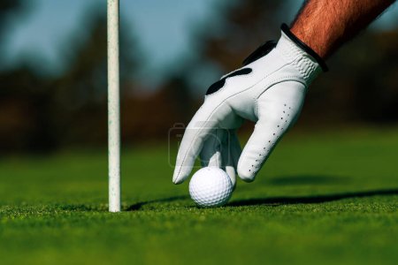 Golfer man hand with golf glove. Golf ball near hole. Golf ball on lip of cup on grass background