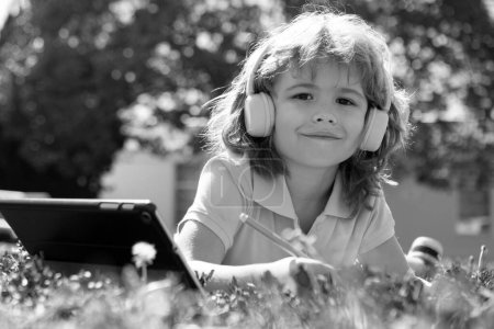 Foto de Lindo niño de la escuela americana en línea de aprendizaje, libro de escritura en el parque. Estudio al aire libre - Imagen libre de derechos