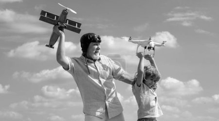 Téléchargez les photos : Jeune petit-fils et vieux grand-père avec avion et drone quadcopter sur fond bleu ciel et nuages. Aîné parent âgé avec enfant - en image libre de droit