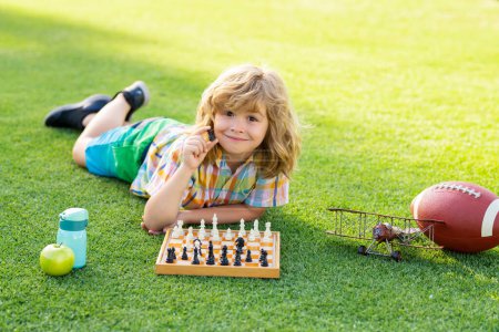 Foto de Juegos de primavera y actividades al aire libre para niños. Escuela de ajedrez exterior. Niño acostado en la hierba en el parque de primavera y pensar en el juego de ajedrez. Concepto de educación infantil - Imagen libre de derechos