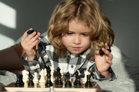 Téléchargez les photos : Intelligent concentré et pensant enfant jouant aux échecs. Jeu d'échecs avec des enfants à la maison - en image libre de droit