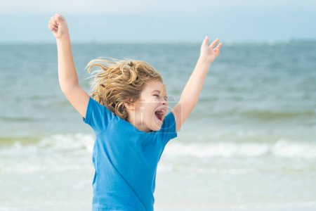 Photo for Excited child face. Excited child run on summer beach. Cute kid raised hand running on the beach enjoying sea. Excited child with raised hand run on sea summer beach. Expressive emotional face - Royalty Free Image