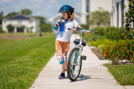 Téléchargez les photos : Enfant à vélo dans un casque. Enfant avec un vélo pour enfants et un casque de protection. Articles sur la sécurité et les sports et activités pour enfants. Garçon heureux d'avoir du plaisir dans le parc d'été avec un vélo - en image libre de droit