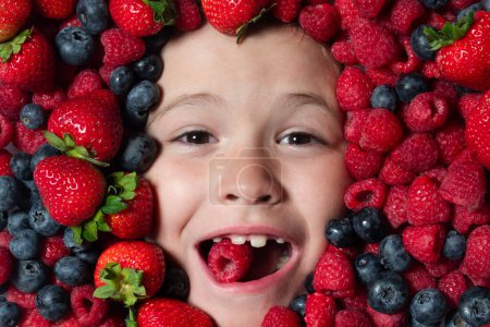 Téléchargez les photos : Les fruits sont prêts. Visage enfant aux baies mélange de fraises, bleuets, framboises, mûres - en image libre de droit