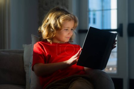 Photo for Elementary school nerd boy pupil read book. Cute kid in casual clothes reading a book while lying on a sofa in the room - Royalty Free Image