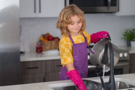 Téléchargez les photos : Lave-vaisselle pour enfants dans la cuisine intérieure. Un enfant qui aide au ménage. Nettoyage et entretien ménager concept. Poussière et gants pour enfants pour le nettoyage - en image libre de droit
