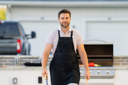 Photo for Man cooking meat on barbecue in the backyard of the house. Handsome man preparing barbecue. Barbecue chef master. Man in apron preparing delicious grilled barbecue food, bbq meat. Grill and barbeque - Royalty Free Image