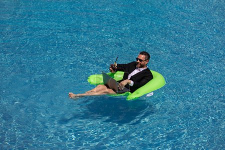 Photo for Funny business man in a business suit floating in the water in the pool. Remote summer work online. Crazy freelancer. Business and summer. Business man drink summer cocktail and using laptop in pool - Royalty Free Image