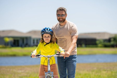 Téléchargez les photos : Joyeuse fête des Pères. Père et fils sur le vélo. Père et fils en vélo dans le parc d'été. Enfant apprenant à faire du vélo. Père et fils à vélo portant des casques. Enfant à vélo extérieur - en image libre de droit