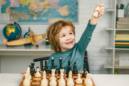 Photo for Thinking child. Kid Playing Chess. Cheerful smiling little boy sitting at the table and evincing gladness while playing chess - Royalty Free Image