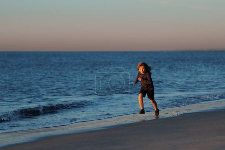 Photo for Little boy child running along ocean. Kid runs on sand beach. Summer vacation with child - Royalty Free Image
