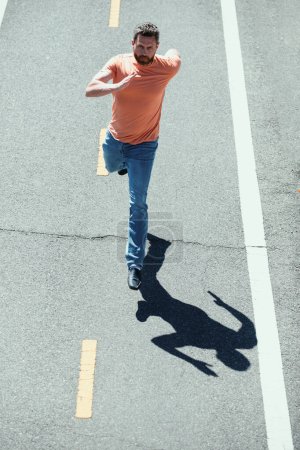 Foto de Un hombre corriendo por la carretera. Joven atlético corriendo en la ciudad. Hombre corriendo por la carretera del campo, entrenamiento de motivación deportiva. Concepto de corredor o corredor - Imagen libre de derechos