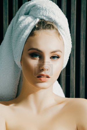 Photo for Portrait of sensual woman with a towel wrapped around her head looking at camera. Beautiful lady drying her hair with white towel after shower - Royalty Free Image