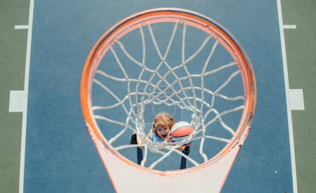 Téléchargez les photos : Un gamin qui joue au basket. Garçon joyeux joueur de basket-ball tenant la balle de jeu - en image libre de droit